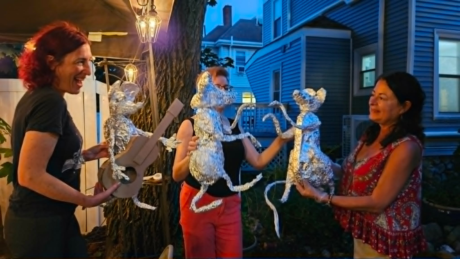 Participants in the public workshop holding their hand-made foil rat sculptures at dusk