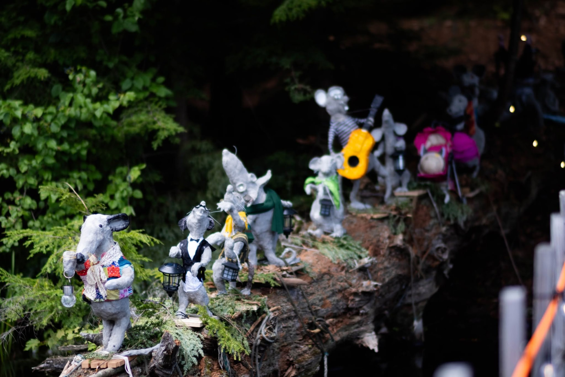 Daylight view of the installation: a procession of hand-made rat sculptures walking a fallen log through the forest