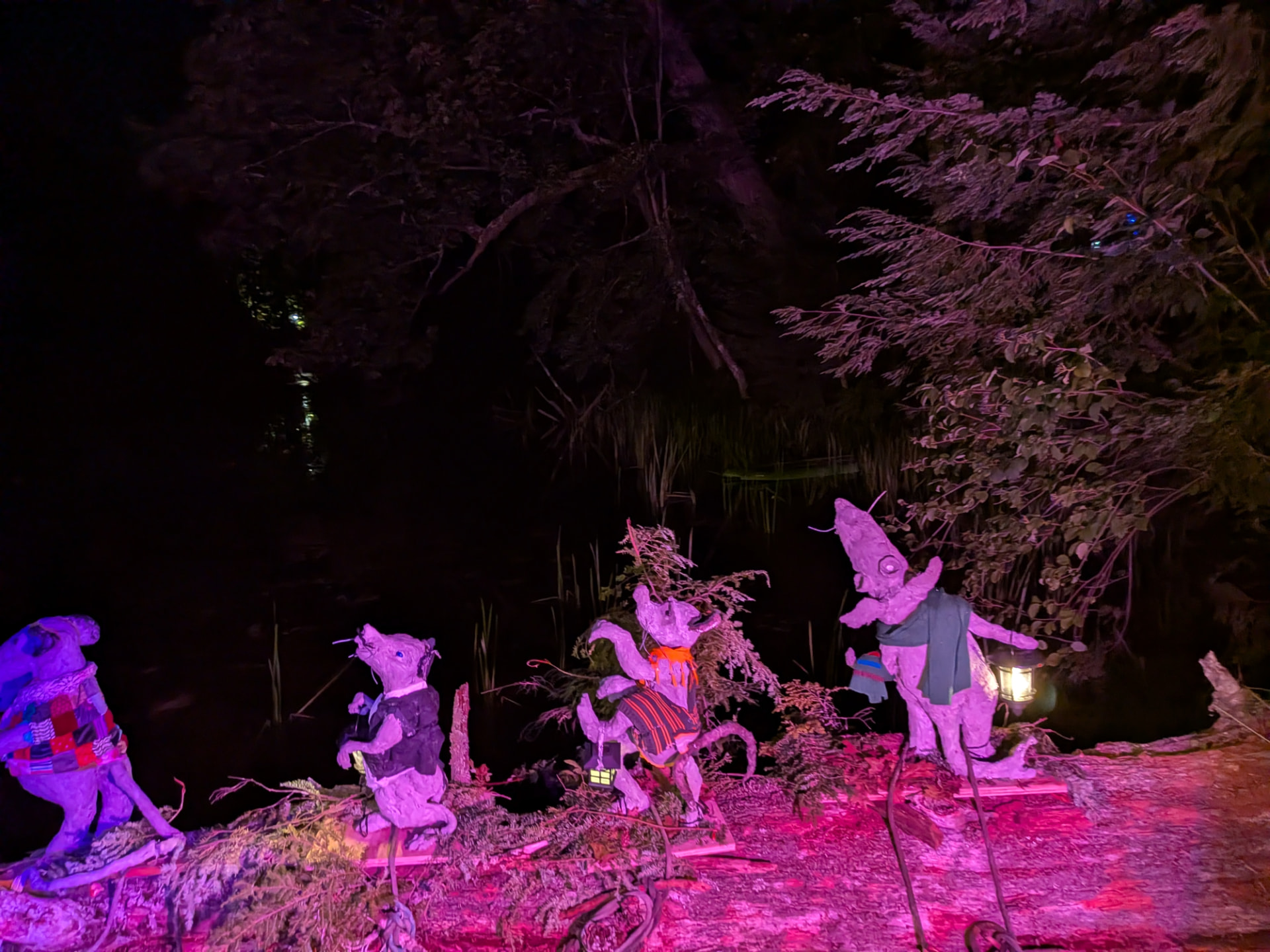 Rat sculptures on a log washed in magenta light, one holding a lantern